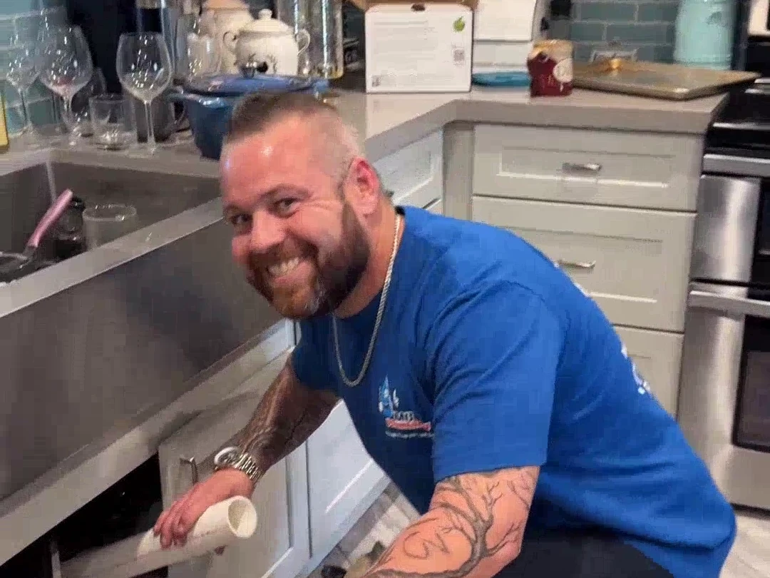 An MC Plumbing crew member beside an open sink cabinet.